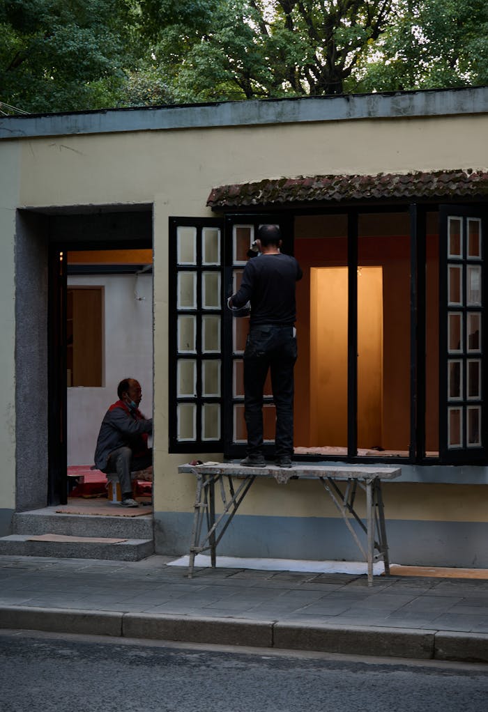 Two workers engaged in home renovation, focusing on repairing windows outdoors.